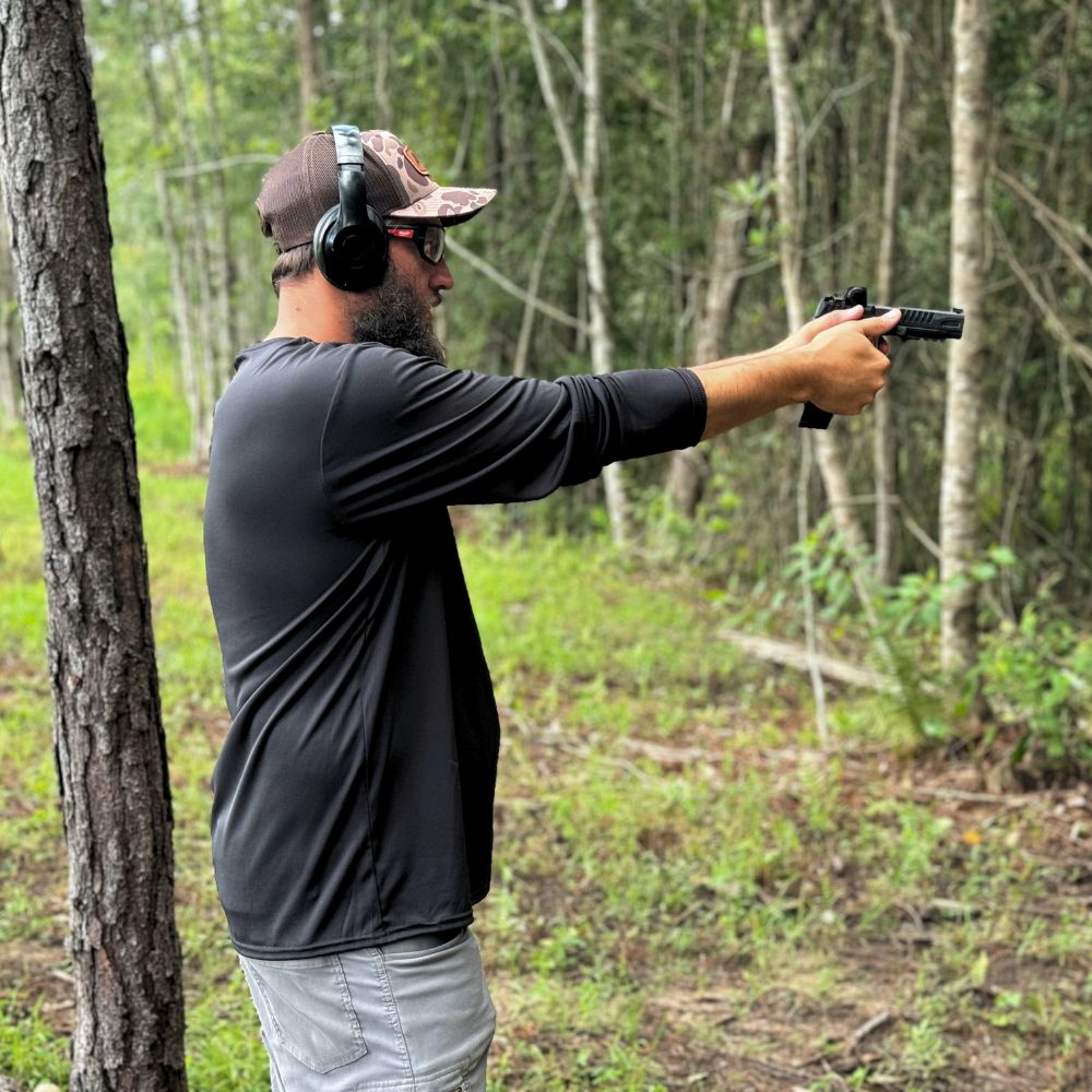 Man in a forest holding a handgun with ear protection
