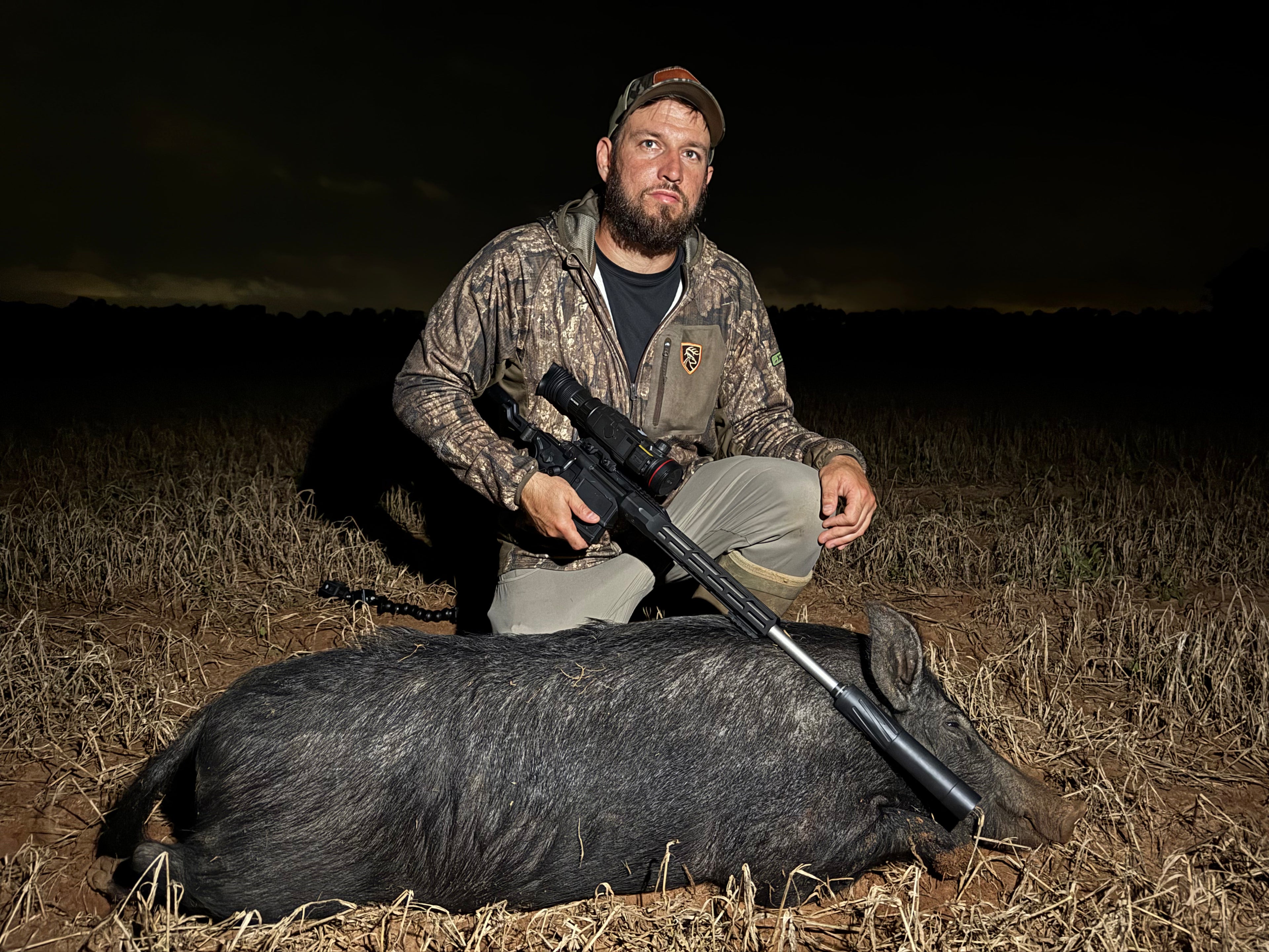 Man with a rifle posing with a hunted hog at night.